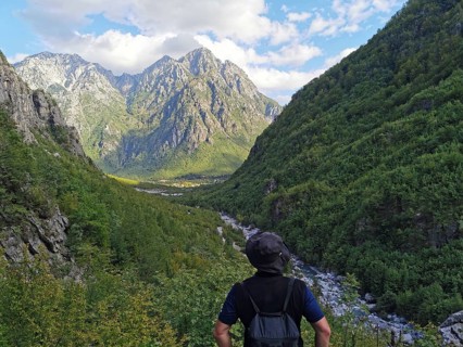 A hiker looks at a wide valley between green mountains, peaceful and impressive nature, peaks of
