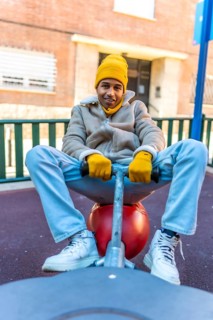 Young man dressed in winter attire happily riding a spring rider in an urban playground, embracing
