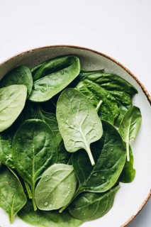 Fresh green spinach leaves with glistening dewdrops on a round, neutral-toned ceramic plate,
