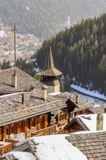 Snow-covered roofs of old farmhouses and barn storage, in the back the large wooden cross and the