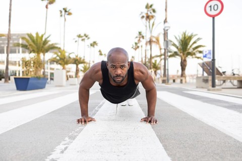 A fit cuban man performs push ups on a city street, surrounded by palm trees and urban scenery. He