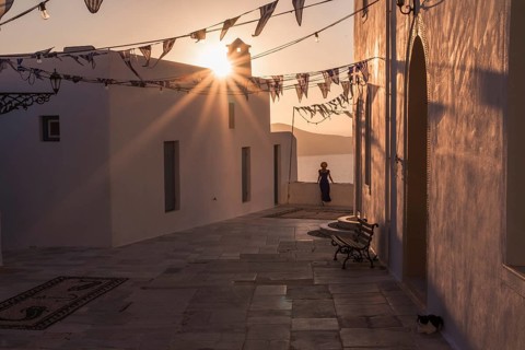 A woman in serene greek village at sunset, with warm sunlight casting long shadows on whitewashed