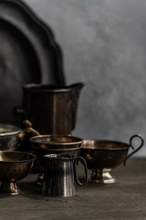 A collection of vintage metal cups and dishes arranged on a textured surface against a muted