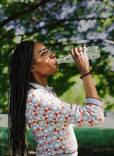 A woman enjoys a sunny day in nature, hydrating with water and capturing the moment with her camera