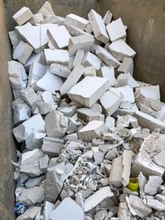 A large container is filled with construction waste from broken white porous concrete or gypsum