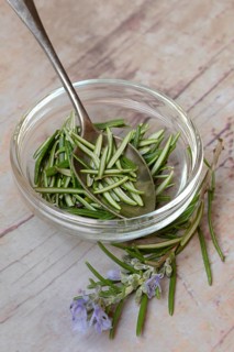 Rosemary, plucked rosemary leaves in a glass bowl and flowering sprig