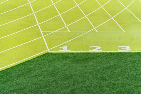 A bright, detailed view of start lines numbered one to three on a green athletics track in an