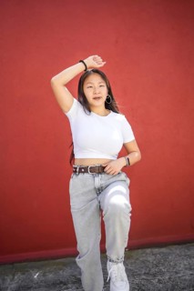Vertical photo of a beauty asian female teenager dancing k-pop in the street against a red wall