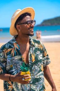 Young man wearing sunglasses and hat, holding a pineapple shaped drink, enjoying the summer sun on