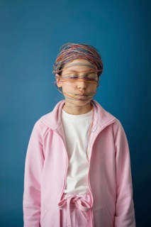 A child in a pink outfit is wrapped in colorful wires, symbolizing the entangling effects of the