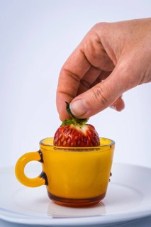 A strawberry dipping into a cup of milk by a woman's hand