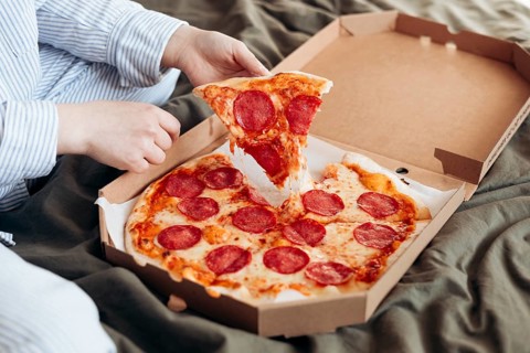 Cropped unrecognizable woman leisurely eating a slice of pepperoni pizza while sitting comfortably