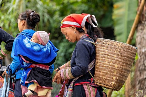 Woman with traditional clothes and carrying basket, carrying child in a shawl. Scenery in a natural