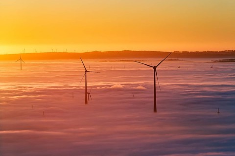 Wind turbines rising from cloud cover, wind farm, silhouettes at sunset, dense sea of fog in the