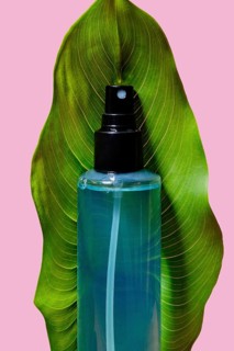 A striking blue cosmetic spray bottle nestled between the curves of a vivid green leaf, highlighted