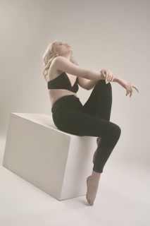 Side view of sensual young female in black bra and leggings tilted her head back while sitting on