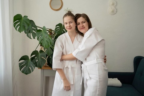 Mother and daughter in white bathrobes share a warm embrace during a self-care session at home.