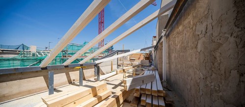A construction site features exposed wooden beams and various building materials under a clear blue