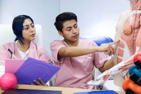 Two physiotherapy students in Ecuador engage in a study session, examining anatomical structures.