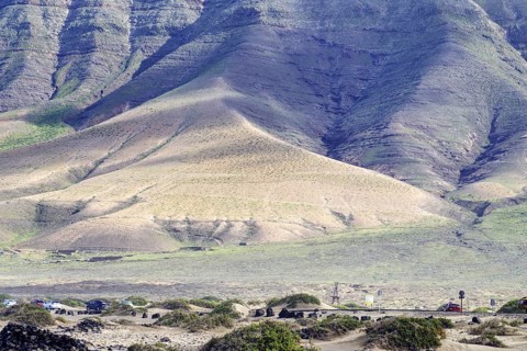 Natural beach with sparse vegetation and road at the foot of the Famara cliffs (Risco de Famara),