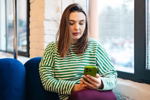 Woman in a striped shirt engrossed in her smartphone while sitting in a cozy cafe. The image