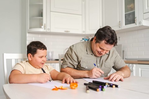 A father and son enjoy drawing together at the kitchen table, surrounded by art supplies and fresh