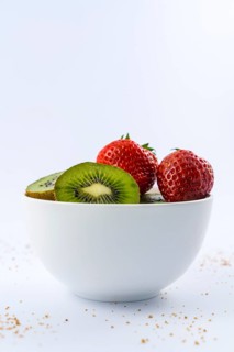 Low view of cut kiwis and strawberries in a white bowl with a white background with brown sugar