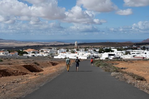 Tourists on a street near Teguise, view of town, white houses of Teguise with church tower,