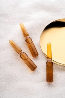 Three brown glass cosmetic ampoules filled with anti-aging serum elegantly displayed beside a