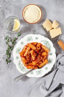 Rigatoni pasta with meat sauce and parmesan cheese on a light table, top view, homemade, no people