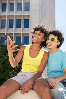 Smiling multiethnic LGBTQ+ couple in bright clothing taking a selfie outdoors with a modern