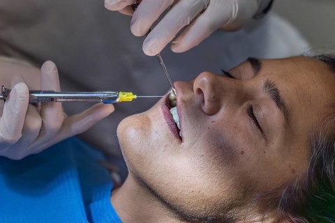 A dentist in gloves performs a teeth cleaning on a patient, administering anesthesia with a syringe