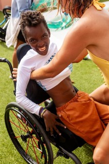 A cheerful wheelchair-bound boy with cerebral palsy in a swimming pool receives loving help from a