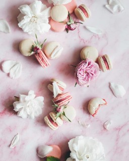 Elegant arrangement of pastel macarons and delicate pink roses on a soft pink marble surface,