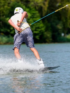 Young man with wakeboard in lake, making turn, water sports, water skiing in wakepark