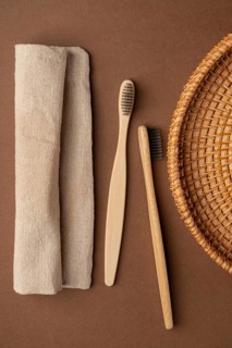 Top view of two bamboo toothbrushes alongside a beige linen towel and a wicker basket, set against
