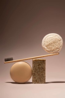 A bamboo toothbrush elegantly balances on a beige soap bar and a natural pumice stone against a
