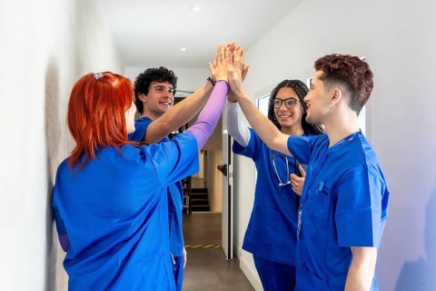 Group of diverse medical students and healthcare professionals in blue uniforms doing a high five