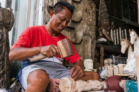 A skilled Indonesian artisan is absorbed in carving a wooden sculpture. His focused expression and