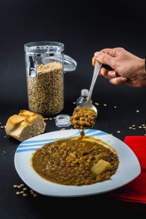 A hand of a young woman eating with a spoon inside a plate of Spanish cooked lentils, along with