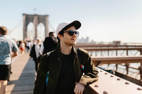 A young man in sunglasses and a cap enjoys a sunny day on a famous city bridge, surrounded by