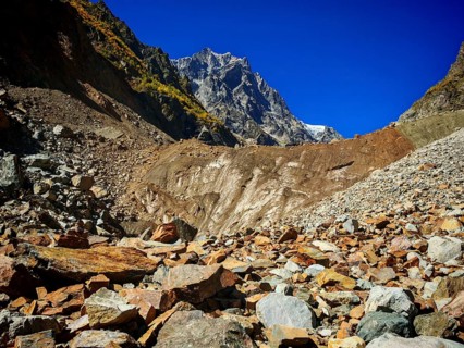 Glacier edge, rugged scree field leading to high mountains under a clear blue sky, hiking to