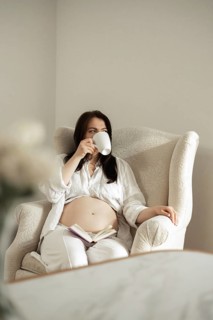 A serene scene of a pregnant woman sitting comfortably in an armchair, savoring a warm drink and