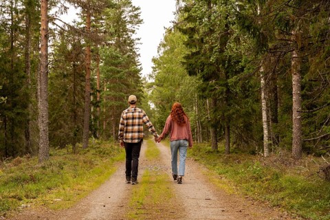 A couple walks down a serene forest path in Sweden, holding hands and enjoying nature. Tall trees