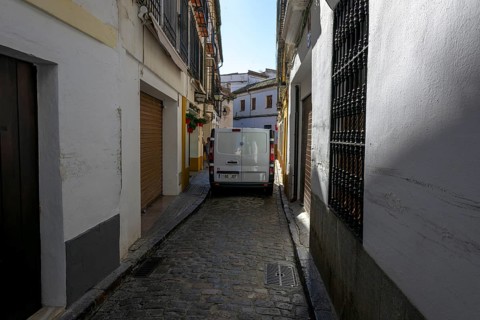 Narrow paved street with parked van between tall, shady walls, Cordoba, Spain