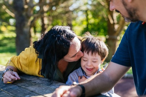 A heartwarming scene of a family enjoying a sunny day outdoors. A woman gently kisses a smiling