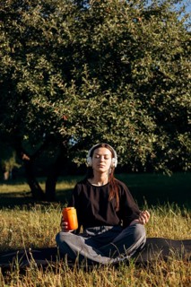 A teenage girl sits peacefully in a lush garden, eyes closed, wearing headphones, meditating or