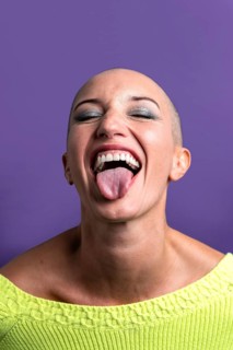 Middle-aged woman with a shaved head joyfully sticks out her tongue, conveying a sense of freedom
