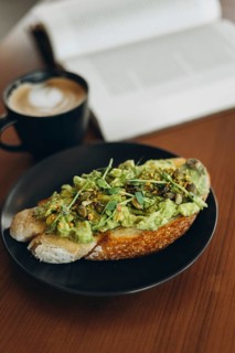 A plate of avocado toast topped with fresh greens and seeds, served alongside a steaming cup of