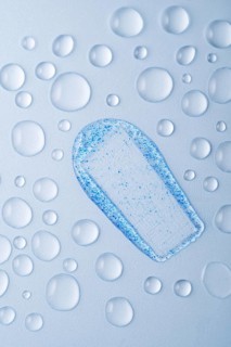 Close-up of a face scrub smear with blue micro-exfoliating particles on a light surface, surrounded